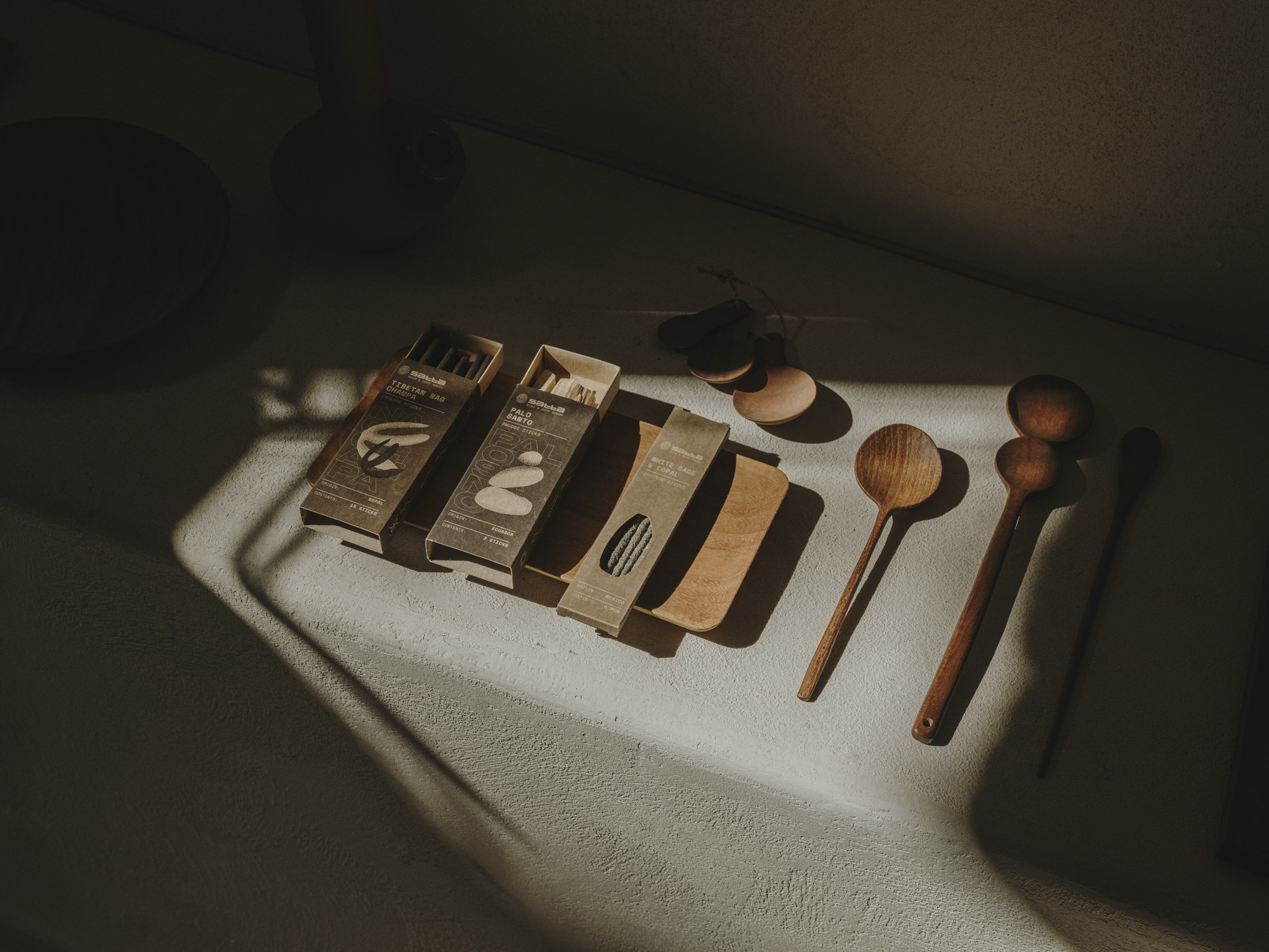 Satta incense boxes and carved wooden spoons on a plaster shelf