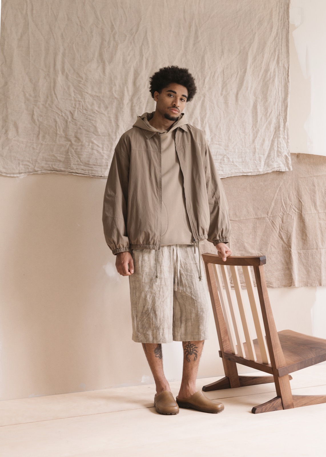 Satta SS25: hooded overshirt and shorts beside a wooden chair