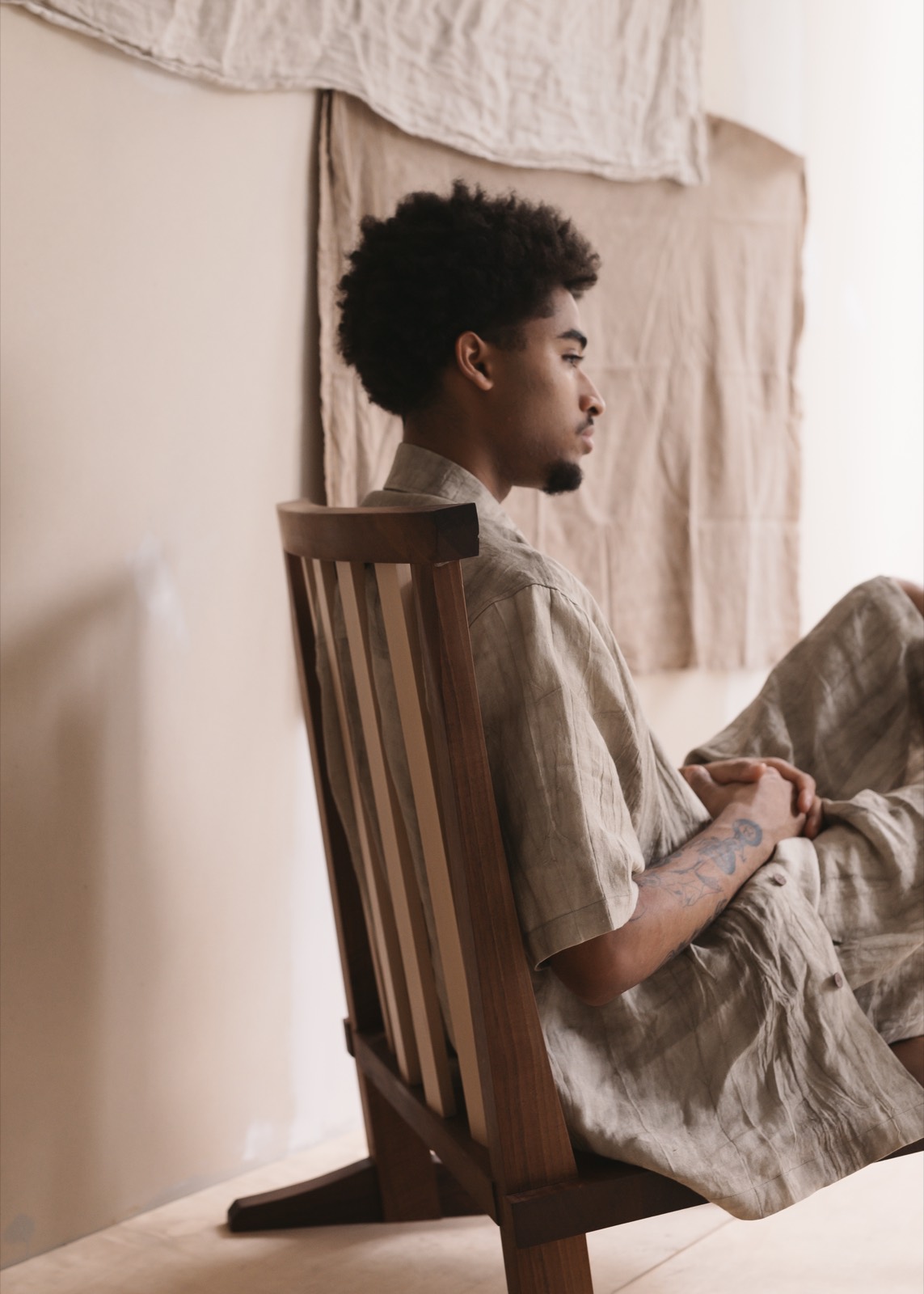 Satta SS25: model seated side-on in a low wooden chair