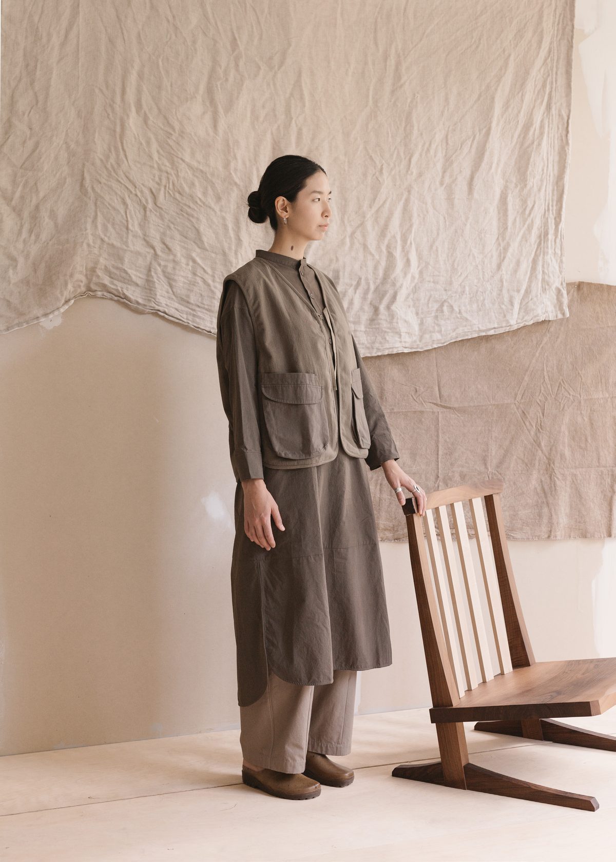 Long utility jacket and trousers beside a low wooden chair